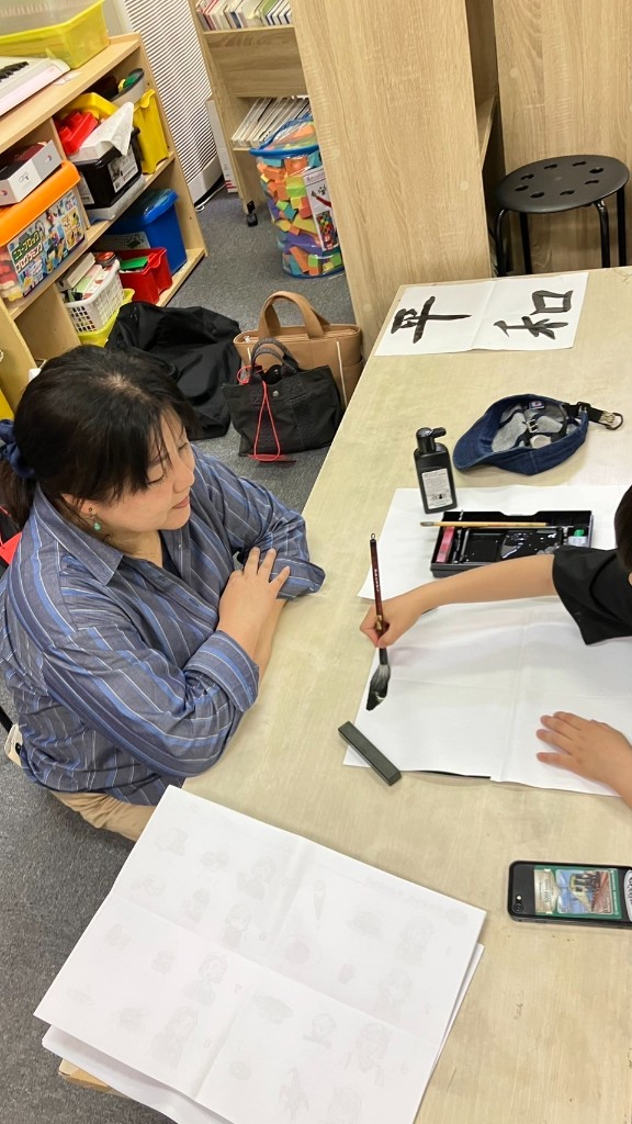 書道の筆で「平和」と書くお子さまを、支援員が見守る様子